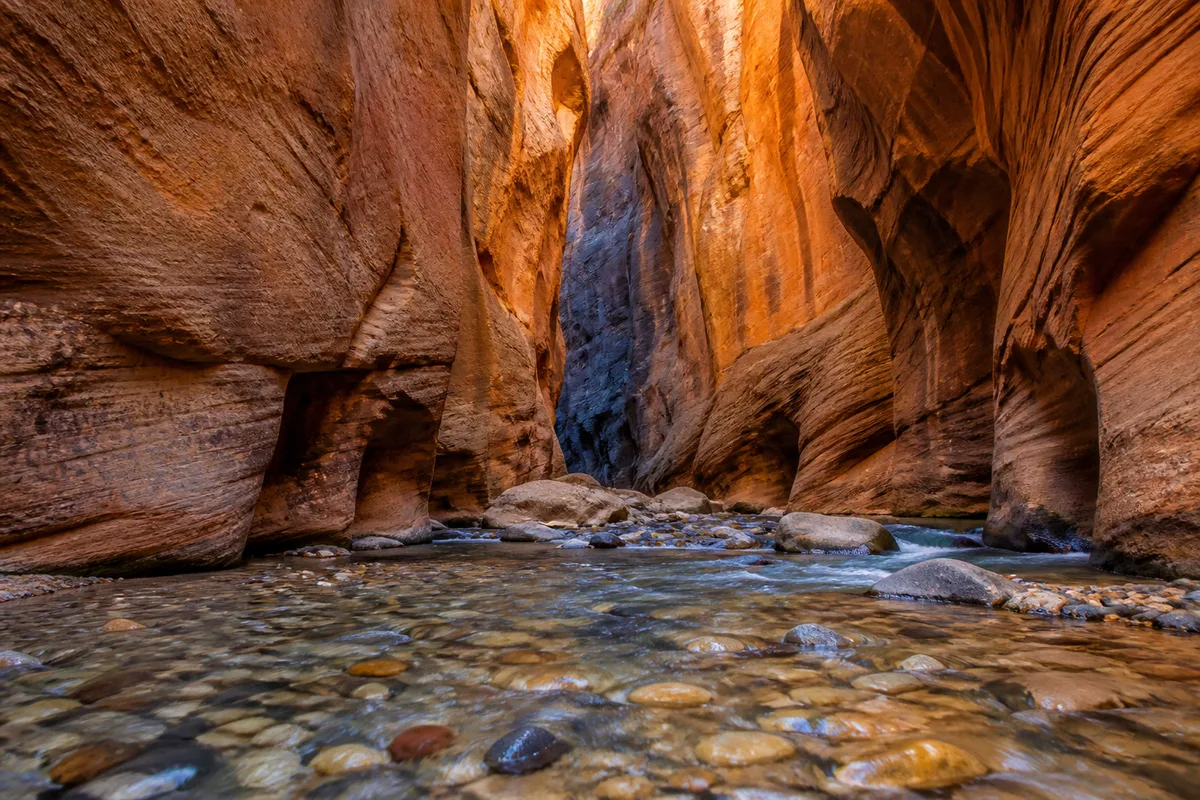 Défilé étroit de grès ocre traversé par une rivière peu profonde, lumière réfléchie sur les parois